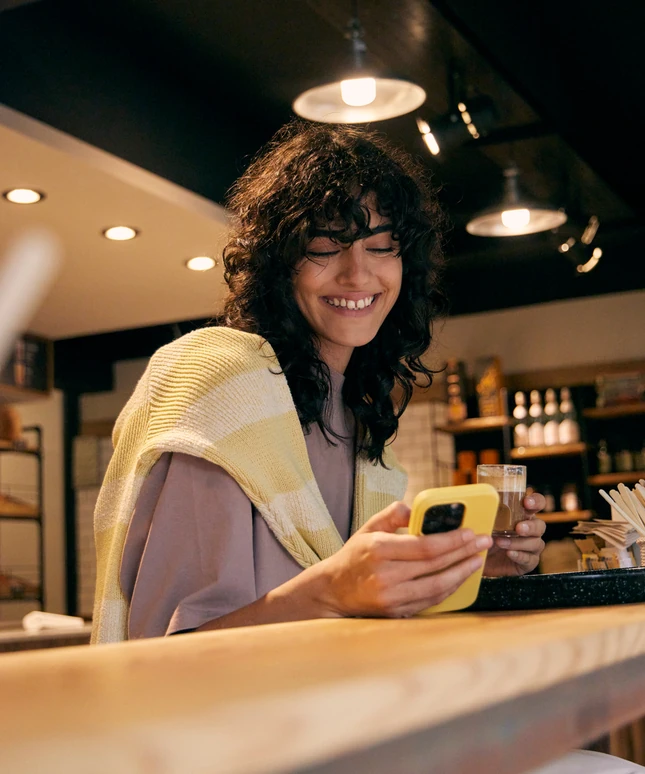 Clienta sonriendo con su celular en la barra de un café